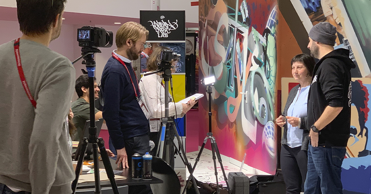 Eine Videocrew nimmt ein Interview an einem Messestand auf.