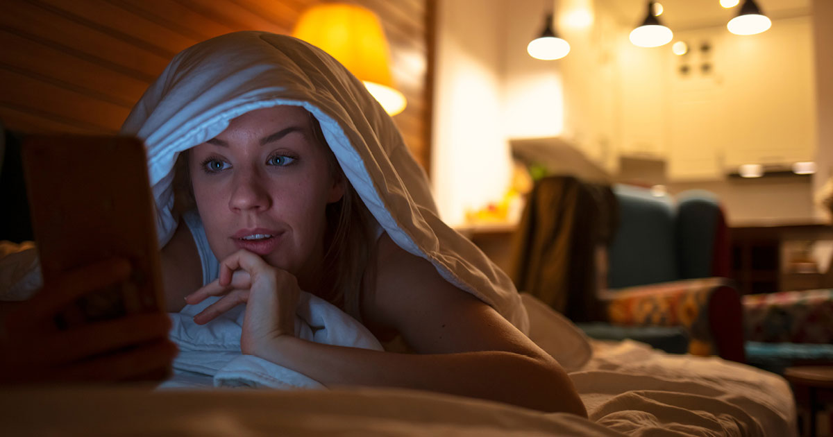 Woman in bed at night reading on her smartphone